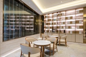 A modern interior with a glass wall, a wall-mounted shelf unit, and a seating area with round tables and chairs. - Ji Hotel (Shanghai)