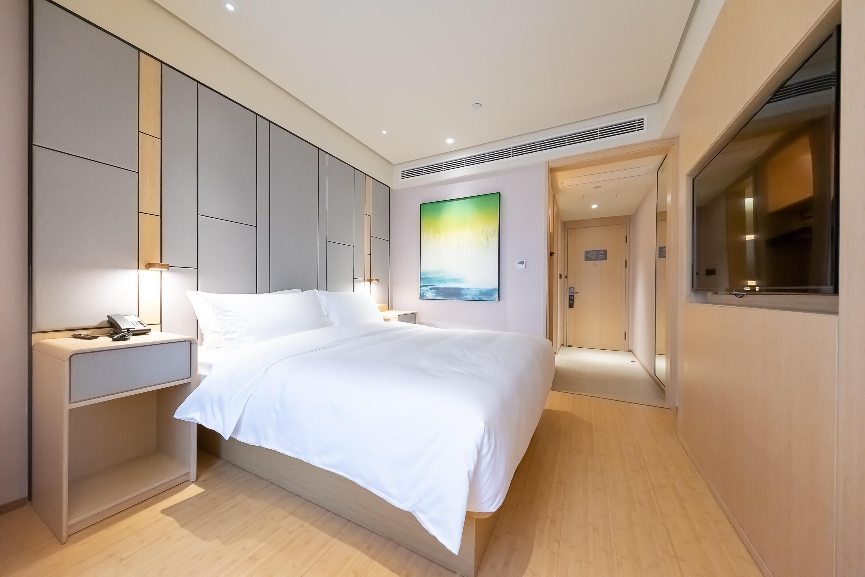 A modern hotel room with a large bed, bedside table, and a painting on the wall.