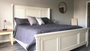 Un lit avec une tête de lit blanche, une literie grise et une table de chevet avec une lampe.