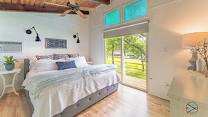 Un dormitorio con una cama grande, un ventilador de techo, una ventana con vista a un parque y una mesita de noche con una lámpara.