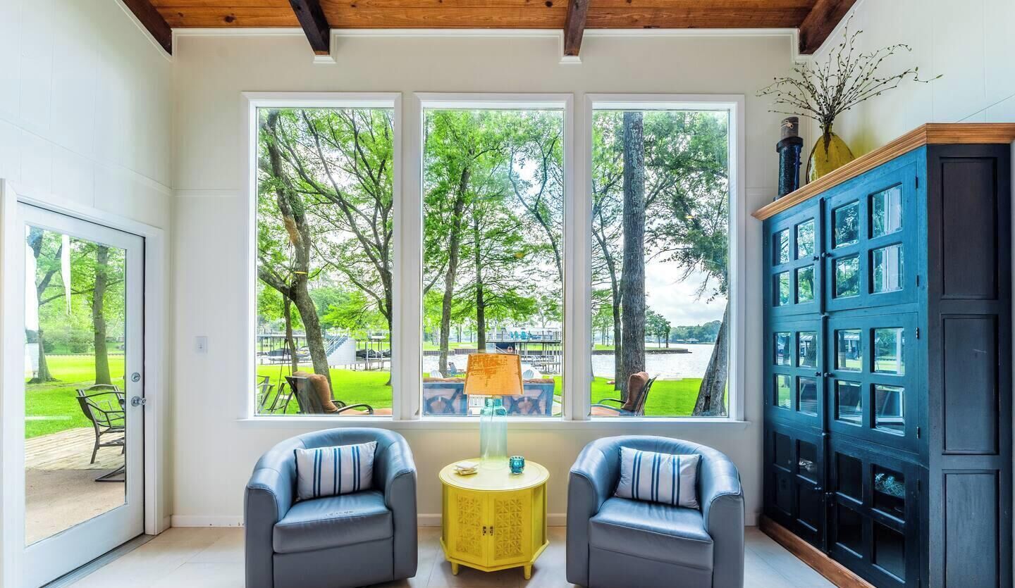 A room with a large window, two chairs, a yellow side table, and a dark blue cabinet.