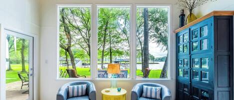 A room with a large window, two chairs, a yellow side table, and a dark blue cabinet.