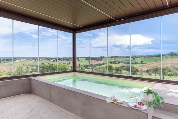 A modern room with a large window, a bathtub, and a table with a book and fruit.