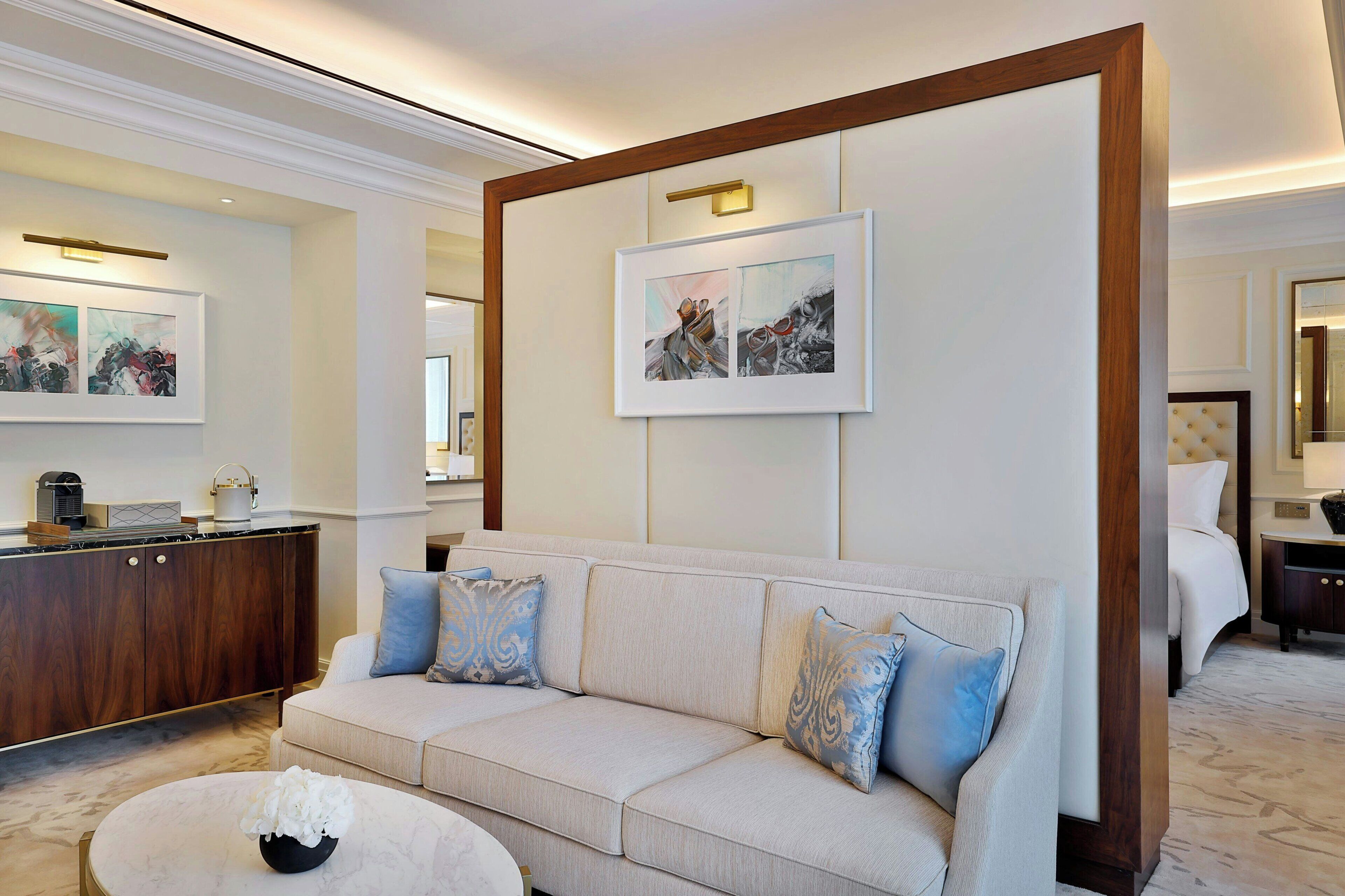 A hotel room with a beige sofa, a marble coffee table, and artwork on the walls.