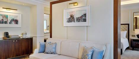 A hotel room with a beige sofa, a marble coffee table, and artwork on the walls.