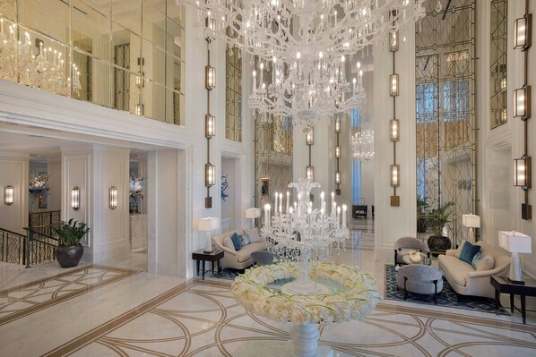 Un vestíbulo amplio con una gran araña, muebles elegantes y un arreglo floral decorativo.