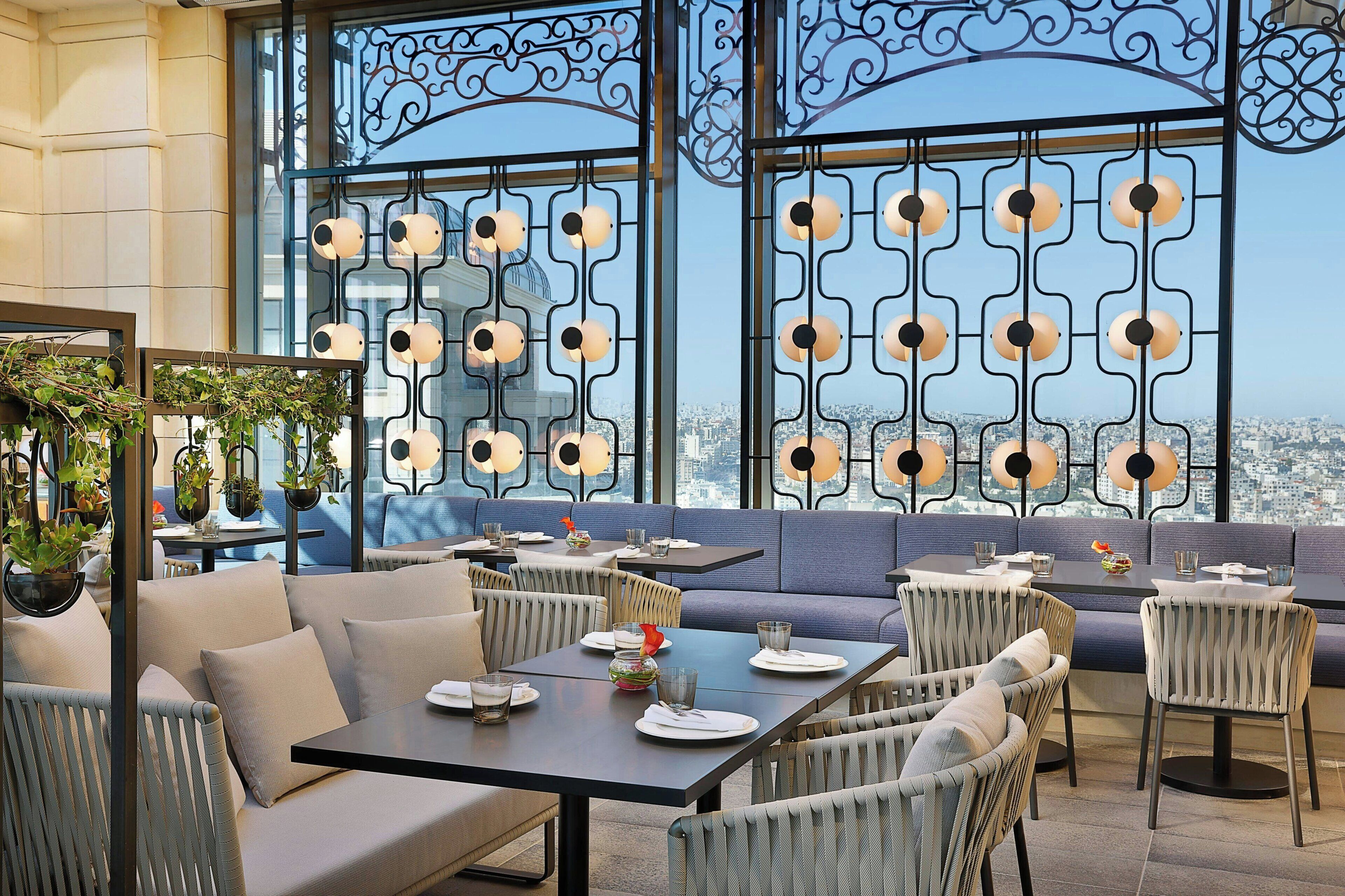 A rooftop restaurant with outdoor seating, large windows, and a city view.