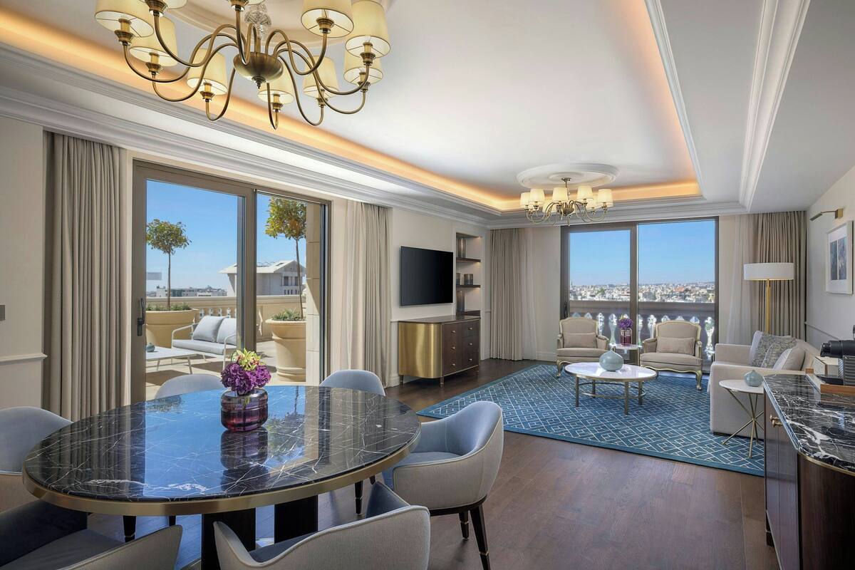 Un salon spacieux avec une table à manger ronde, des sièges confortables, un grand téléviseur et une vue sur la ville.