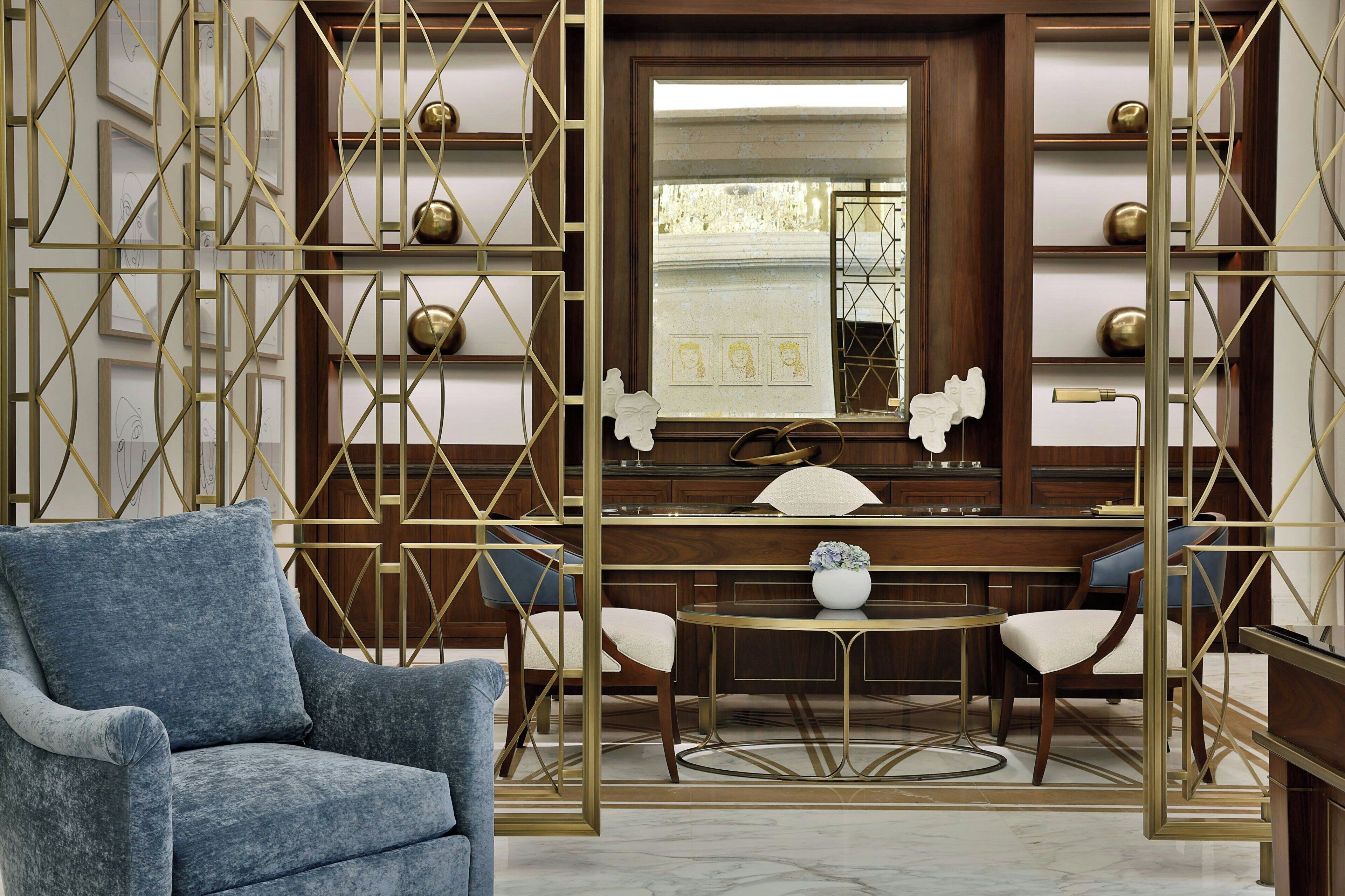 A modern interior with a blue armchair, a wooden dining table with chairs, and decorative gold geometric patterns.