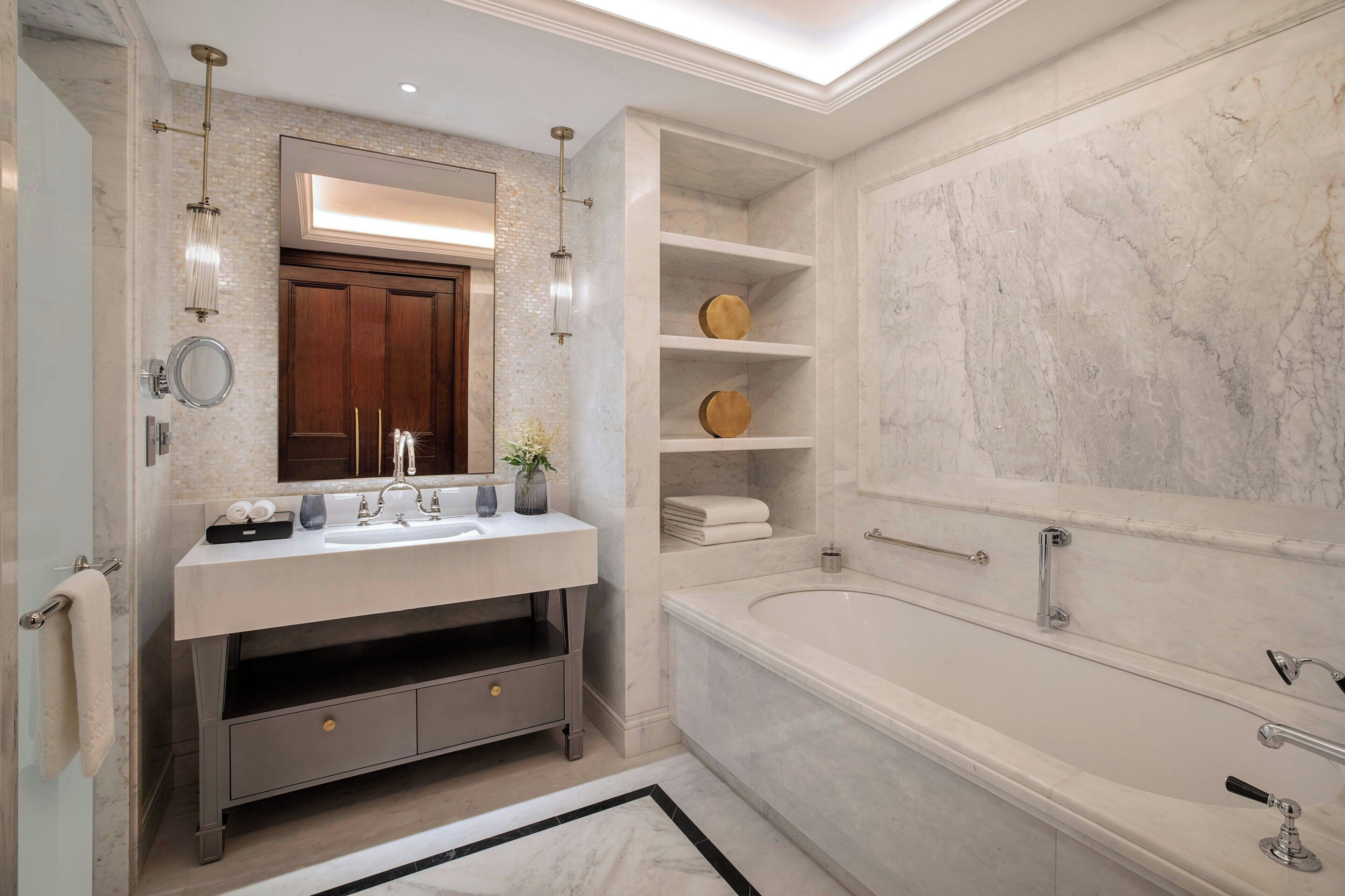 Un baño moderno con lavamanos de mármol, una bañera grande y estantes empotrados.