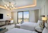 A hotel room with two beds, a desk, a TV, and a view of the city.
