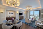 A hotel room with a dining area, a sofa set, a TV, and a large window with a city view.