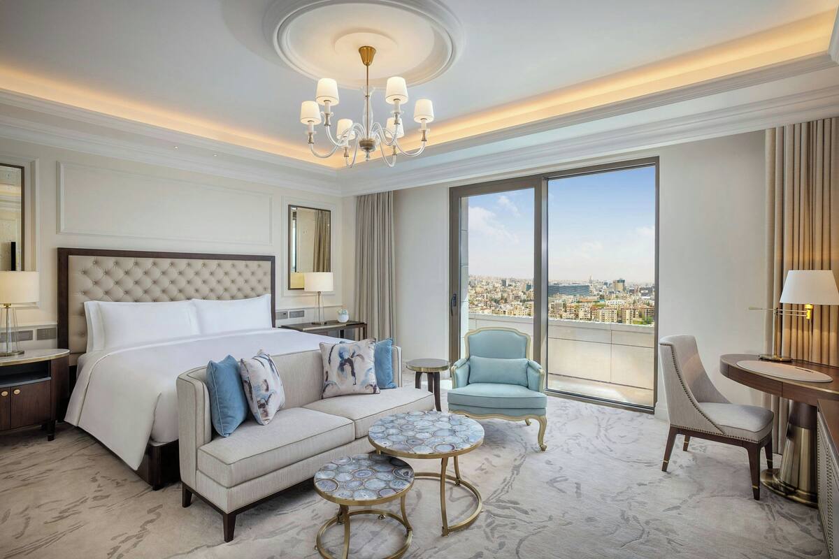Une chambre d’hôtel spacieuse, dotée d’un grand lit, d’un canapé, de deux petites tables rondes, d’une chaise et offrant une vue sur la ville.
