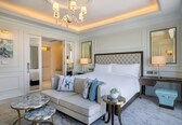 A hotel room with a large bed, a sofa, a small round table, and a desk with a lamp.