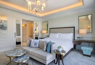 A hotel room with a large bed, a sofa, a small round table, and a desk with a lamp.