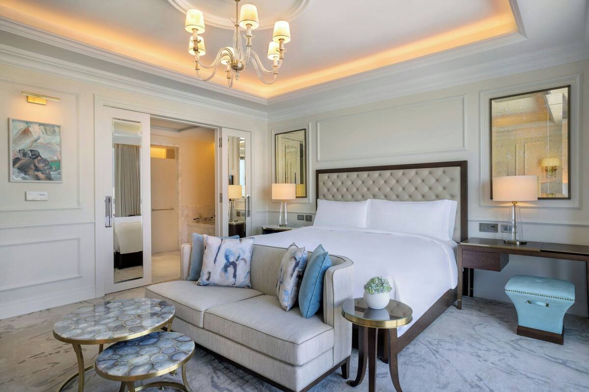 Une chambre d’hôtel avec un grand lit, un canapé, une petite table ronde et un bureau avec une lampe.