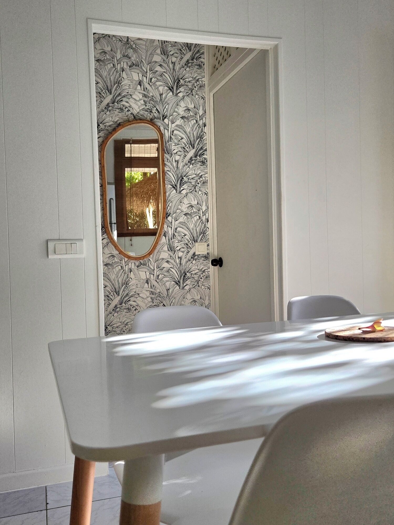 A dining area with a white table and chairs, a mirror on the wall, and a door with a floral wallpaper.
