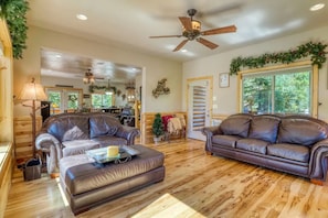 A spacious living room with two leather sofas, a coffee table, and a ceiling fan.