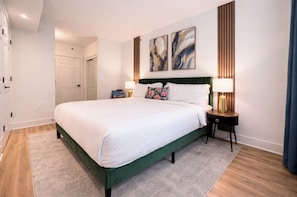 Ett hotellrum med en stor säng, två sänglampor och en dörr som leder till ett annat rum.