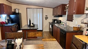 A compact kitchen with wooden cabinets, a refrigerator, stove, and a sink. There is a dining table with chairs and a rug. - Nice and Cozy cabin, 3 bedroom and 2 bathroom. (Ruidoso)