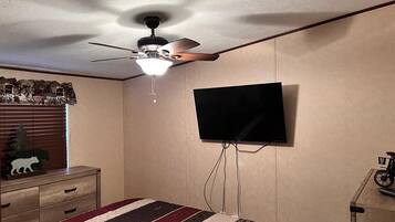 A bedroom with a bed, a ceiling fan, a mounted TV, a dresser, and a window with blinds.