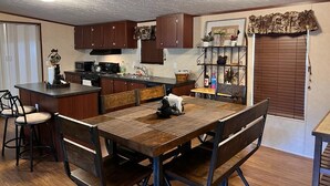A compact kitchen with wooden cabinets, a central island, and a dining area with a table and chairs. - Nice and Cozy cabin, 3 bedroom and 2 bathroom. (Ruidoso)