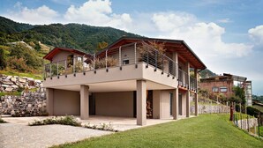 Une maison moderne à deux étages, dotée d’un toit plat, d’un balcon et d’un mur en pierre en arrière-plan.