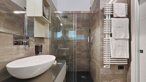 Une salle de bain moderne avec un grand lavabo blanc, une douche à parois de verre et un porte-serviettes muni de plusieurs serviettes.