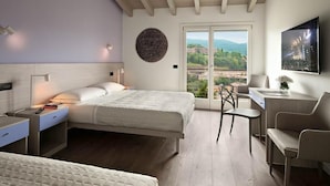 Une chambre à coucher comprenant un lit, des tables de chevet, un bureau et une chaise. Une grande fenêtre offre une vue sur l’extérieur.
