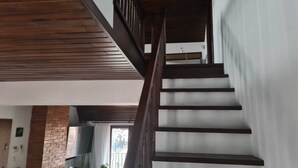 Eine Treppe mit Holzdielen und dunklen Geländern, die zu einem Zwischenpodest mit weißer Wand und einem Fenster führt.