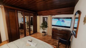 Ein Schlafzimmer mit einem Bett, einer Holzkommode, Topfpflanzen, einem Fernseher und einem Spiegel.
