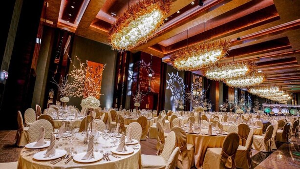 Ein Bankettsaal mit runden Tischen, gedeckt für ein Essen, jeweils mit weißen Tischdecken und goldenen Stühlen.
