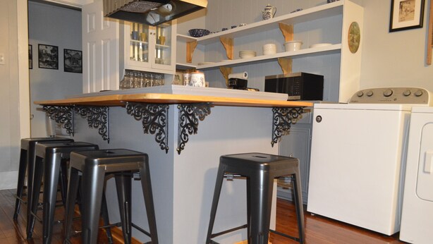 Una cocina con una isla de madera, taburetes de bar, microondas y lavadora.