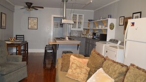 Un espacio habitable compacto con kitchenette, comedor y zona de estar con sofá y sillones.