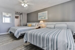 A bedroom with two beds, a ceiling fan, a window, and a painting on the wall.