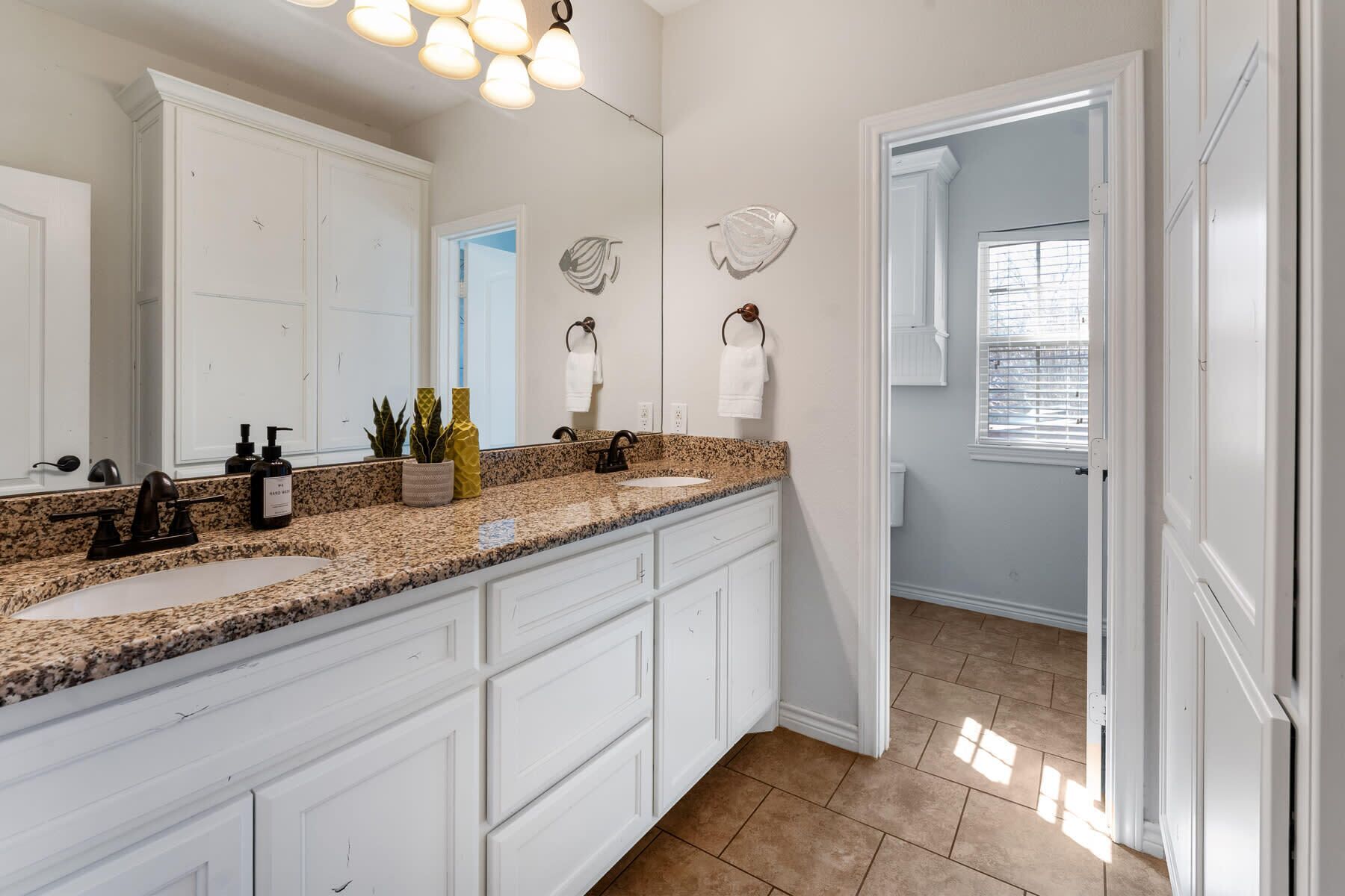A bathroom with white cabinetry, granite countertops, a double sink, and a large mirror.