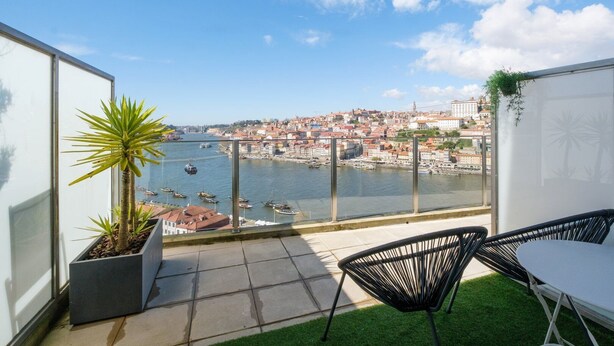 A balcony with a view of a river and cityscape, featuring a chair, a small plant, and a table. - GuestReady - Port Studio 3 (Vila Nova de Gaia)