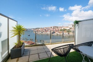 Un balcon offrant une vue sur une rivière et le paysage urbain, avec une chaise, une petite plante et une table.