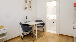 A small, modern room with a white table and two chairs, a wine bottle, and framed pictures on the wall. - GuestReady - Port Studio 3 (Vila Nova de Gaia)