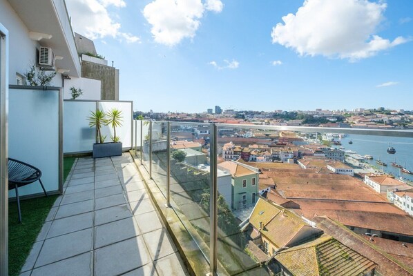 Enjoy the stunning view of the coastal town from this balcony, featuring a tiled floor and glass railing, surrounded by lush potted plants.