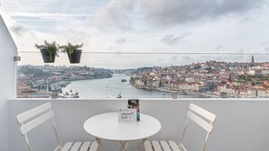 A balcony with two white chairs and a small round table, overlooking a cityscape with a river and historic buildings.