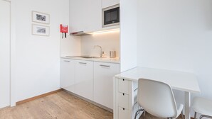 A compact kitchen with white cabinetry, a microwave, a sink, and a small dining area with a chair.
