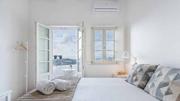 A bedroom with a bed, a window with a view, a bedside table, and a hanging light.