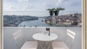 A balcony with two white chairs and a small round table, overlooking a cityscape with a river and buildings. - GuestReady - Port Studio 1 (Vila Nova de Gaia)