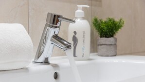 A bathroom sink with a chrome faucet, a white towel, a bottle of soap, and a small potted plant. - GuestReady - Miragaia Stone Studio 1F (Porto)