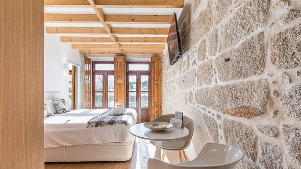 A bedroom with a bed, a round table, and a chair. There are wooden beams on the ceiling and a stone wall. - GuestReady - Miragaia Stone Studio 1F (Porto)