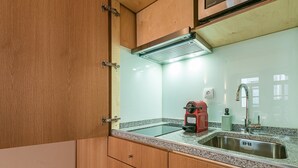 A kitchen with wooden cabinets, a stainless steel sink, a red coffee maker, and a built-in range hood. - GuestReady - Miragaia Stone Studio 2T (Porto)