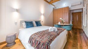 A modern bedroom with a large bed, two wall-mounted lights, a wooden ceiling, a small round table with chairs, and a door. - GuestReady - Miragaia Stone Studio 2T (Porto)