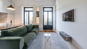 Un salon moderne avec un canapé vert, une petite table blanche et un coin cuisine doté d’un luminaire suspendu.