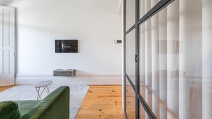 Une chambre moderne dotée d’une porte-fenêtre coulissante, d’un téléviseur à écran plat fixé au mur, d’une petite table avec une chaise et d’un canapé vert.